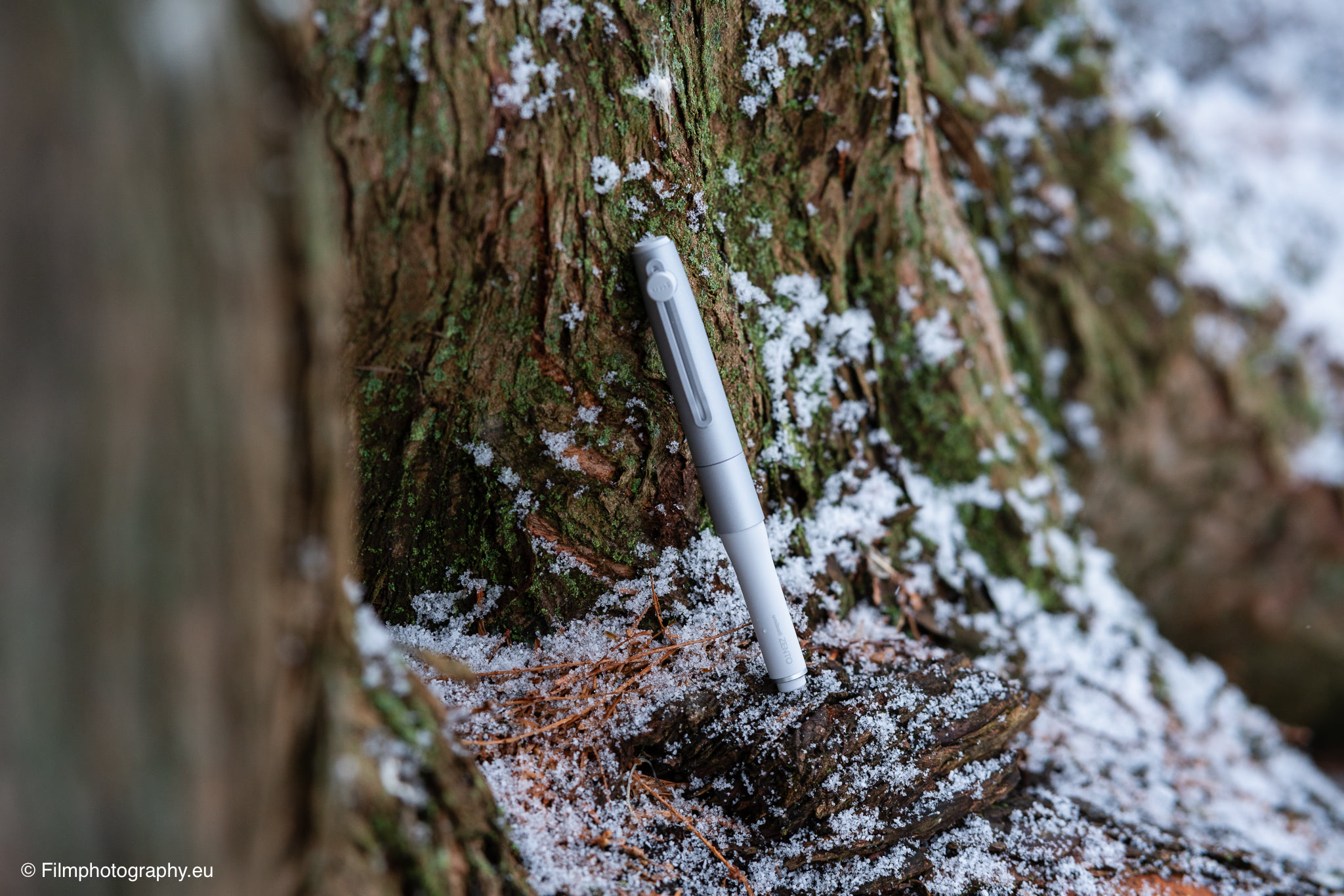Uniball Zento Signature钢笔倚靠在覆满新雪的苔树干上，静谧冬日森林场景