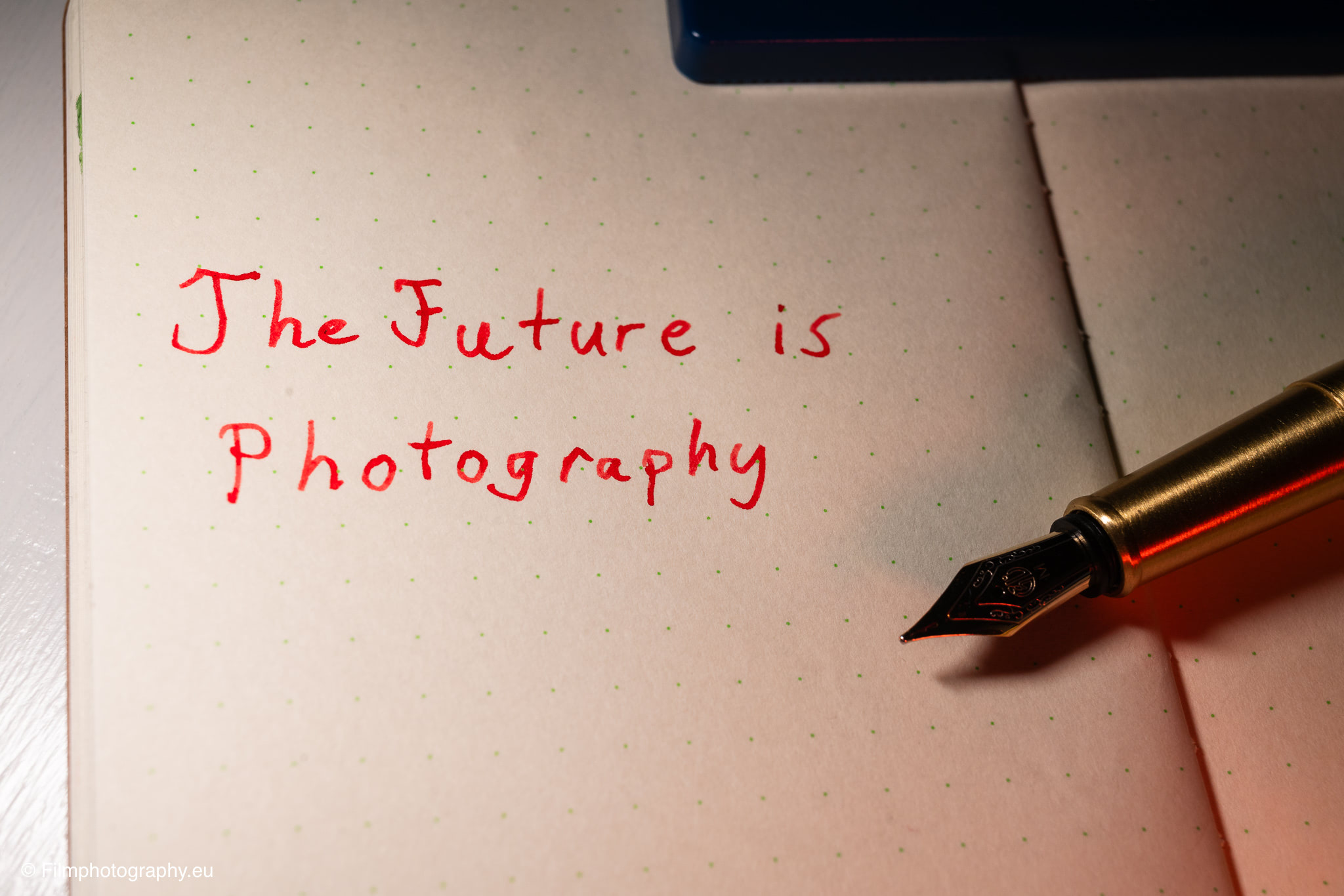 Nahaufnahme eines Yamamoto Robiki Notizbuchs mit The Future is Photography in roter Tinte, eine Messing-Federhalter unter warmem Licht