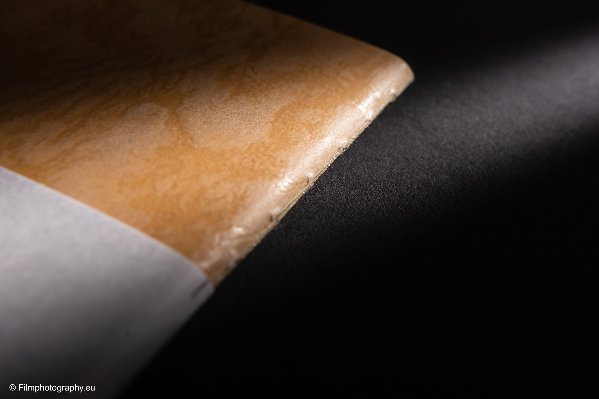 Nahaufnahme eines abgenutzten hellbraunen Leder-Yamamoto-Robiki-Notizbuchs mit weißem Papierstreifen auf dunkler Oberfläche, dramatisches
