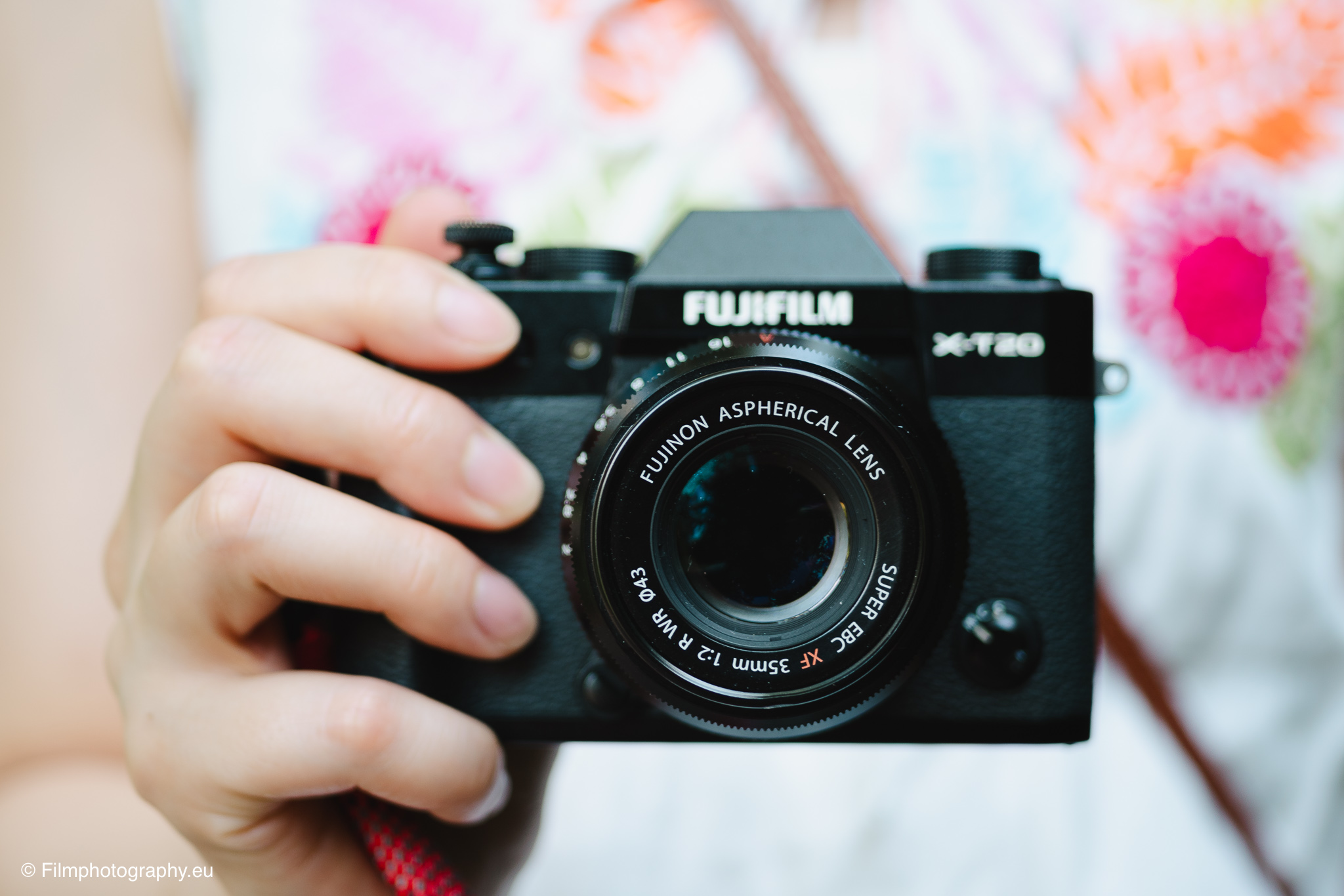 Hand hält Fujifilm X-T20 mit Fujinon XF 35mm f/2 R WR Objektiv, weicher Blumenhintergrund, Objektiv-Review-Fotografie