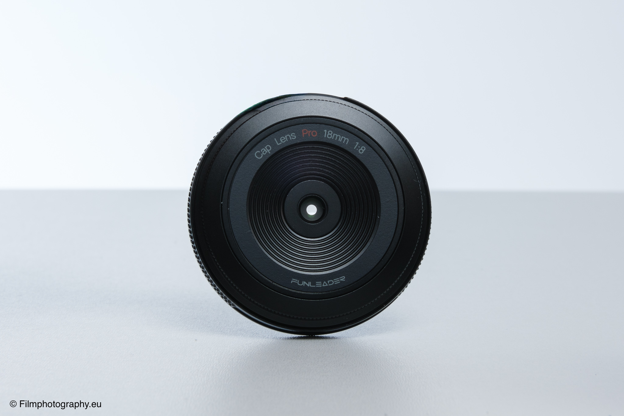 Frontansicht einer Funleader Cap Lens Pro 18mm f/8 Linse auf weißer Oberfläche, kompaktes Design und konzentrische Glaselemente