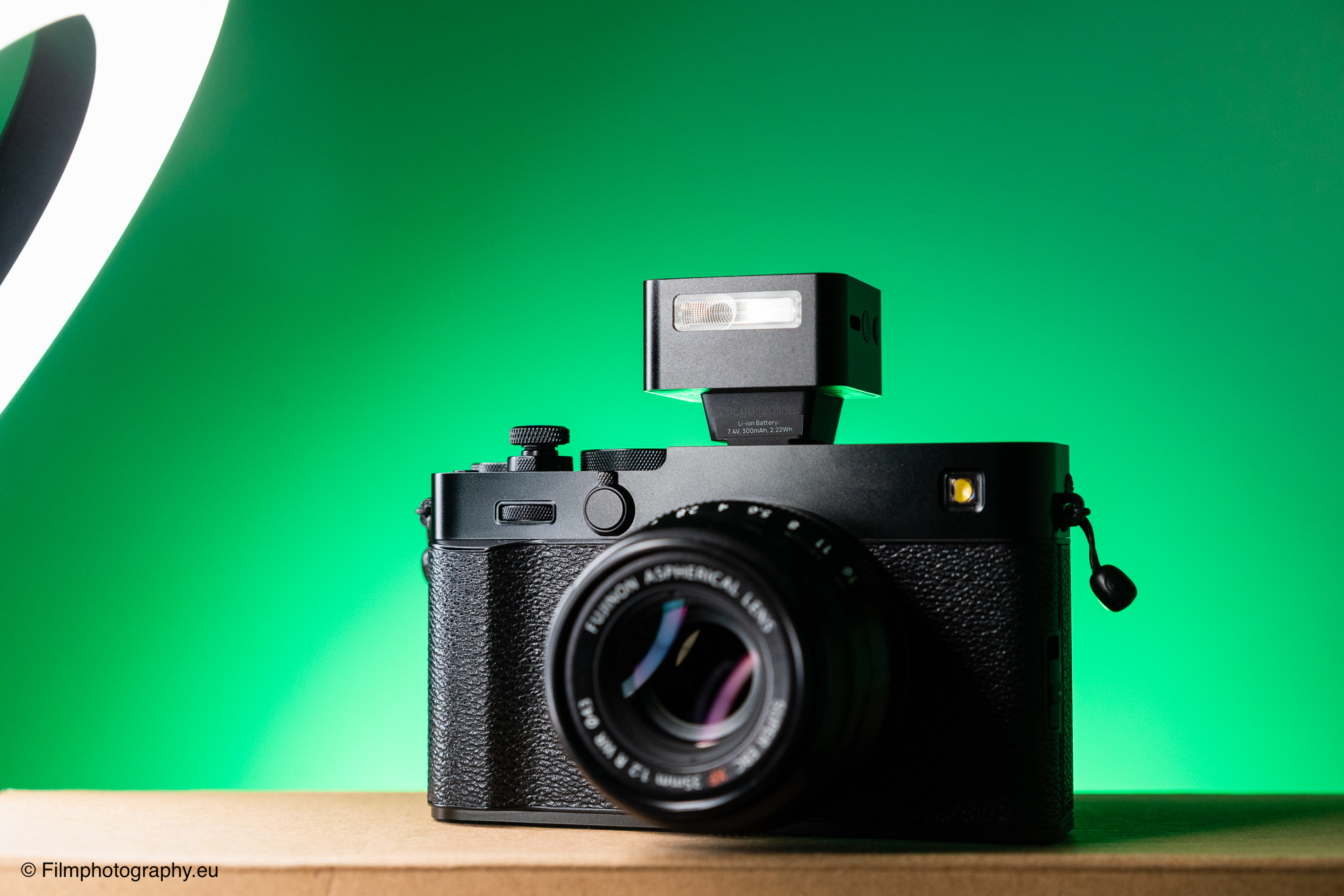 Fujifilm Kamera mit Fujinon Objektiv und Zeniko ZF08 TTL Blitz aufgesetzt auf lebhaft grünem Hintergrund auf Holz