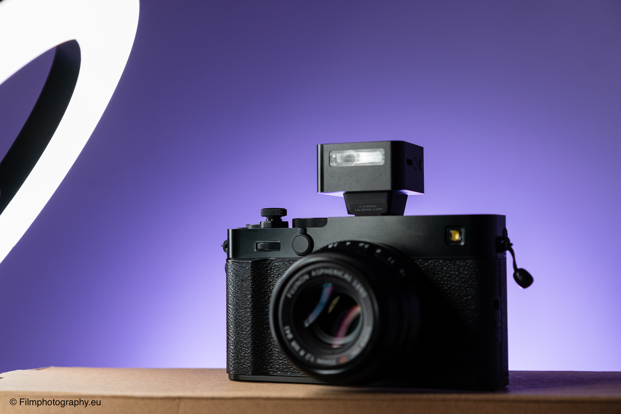 Fujifilm-Kamera mit Zeniko ZF08 TTL-Blitz auf dem Blitzschuh, auf einer Holzoberfläche vor purpurfarbenem Hintergrund