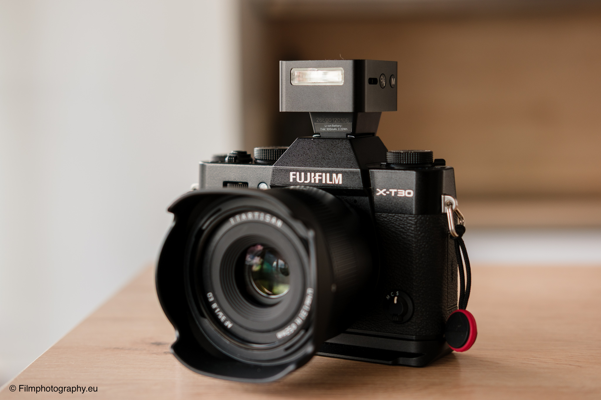 Fujifilm X-T30 mit Zeniko ZF08 TTL-Blitz aufgesetzt, Fujinon-Objektiv mit Linsenblende, auf Holztisch ruhend.