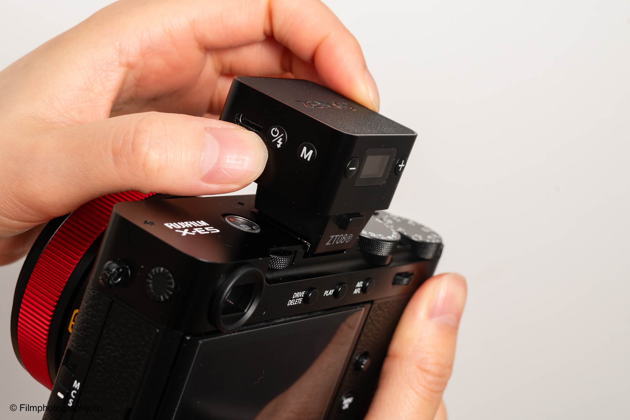 Manuelle Einstellung des Zeniko ZF08 TTL Blitzes an einer Fujifilm X-E5 spiegellose Kamera mit rotem Ringobjektiv, weißer Hintergrund