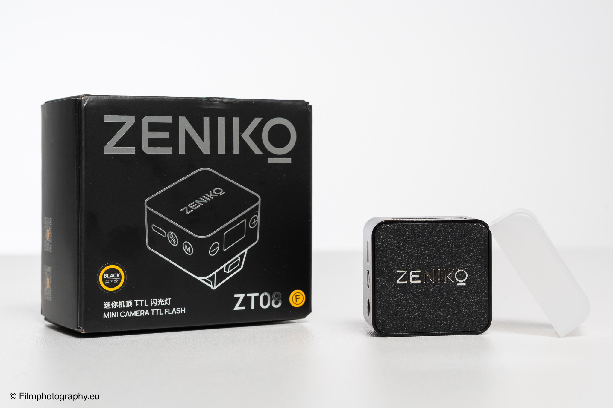 Zeniko ZT08 TTL Blitz für Fujifilm-Kameras neben der schwarzen Verpackung auf weißem Studiohintergrund