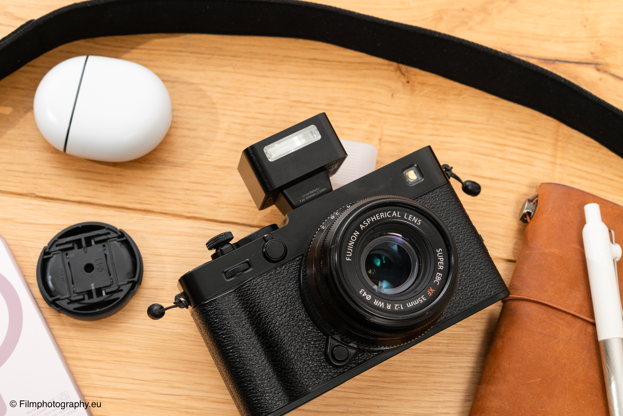 Fujifilm-Kamera mit Fujinon-Asphärischer Linse und Zeniko ZF08 TTL-Blitz oben montiert, auf Holzoberfläche ruhend