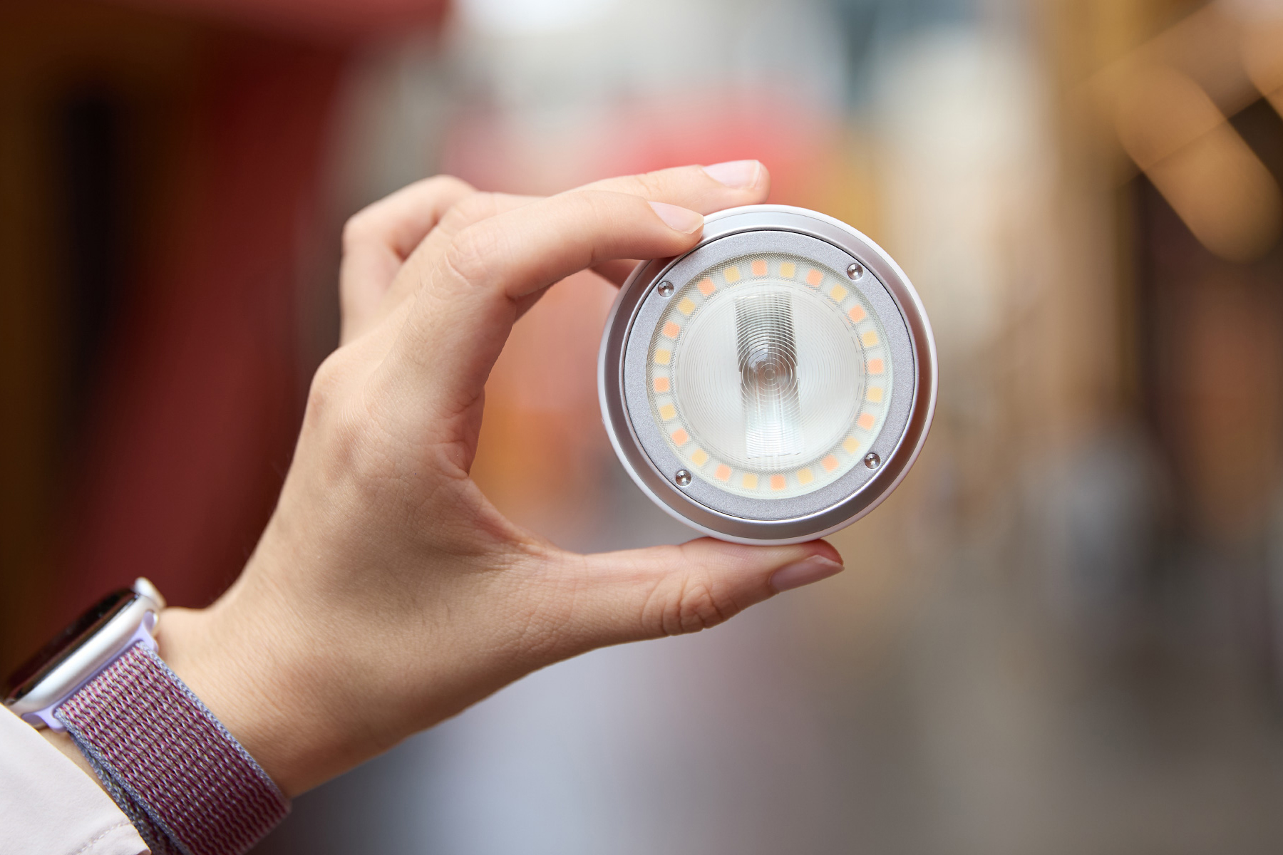 Hand hält das runde Godox A2 Xenon Blitzgerät mit LED-Ring vor verschwommenem Straßenhintergrund, ein smartphonefreundliches Licht für