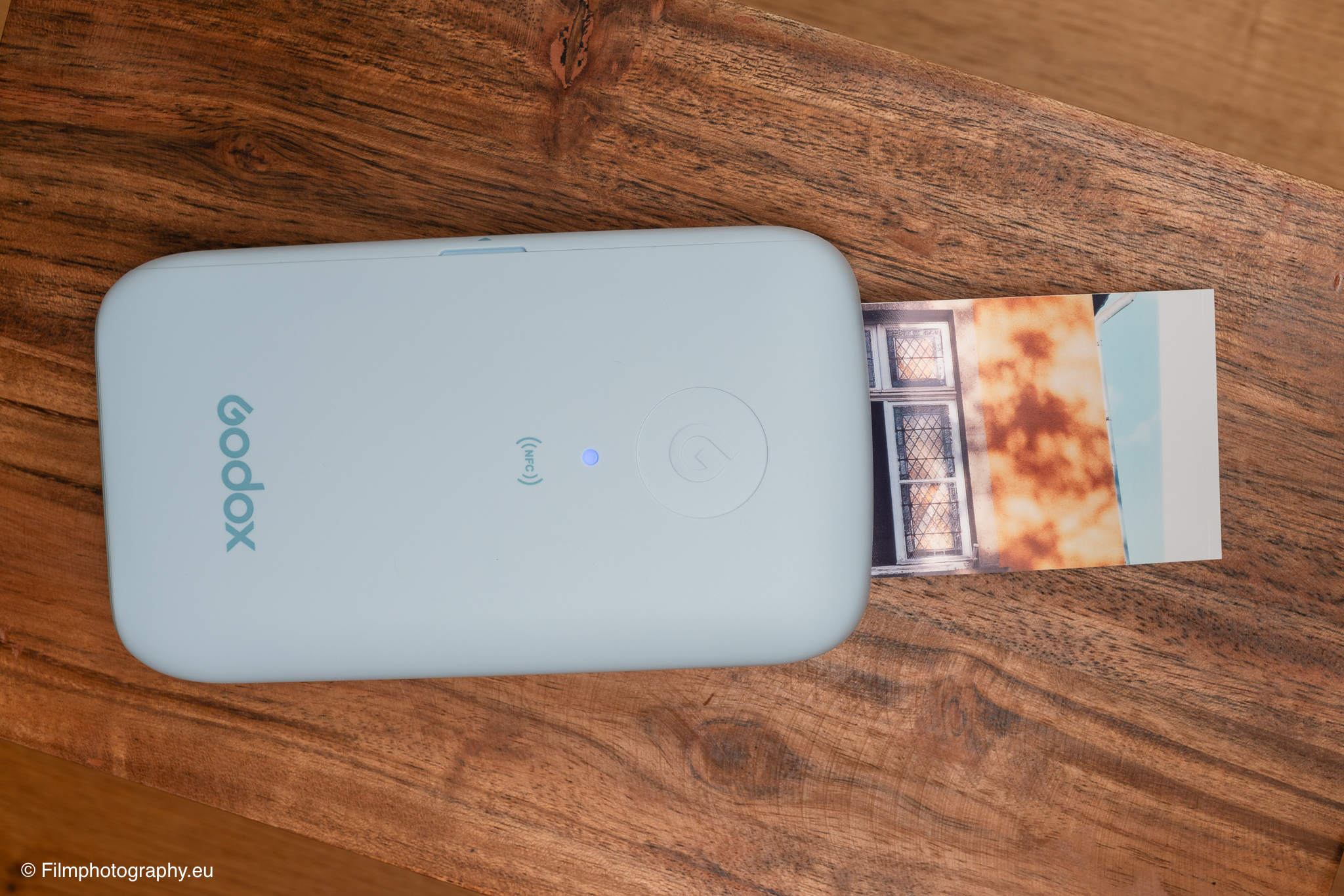 Godox P100 mobiler Fotodrucker in Hellblau stößt einen warmtonigen Ausdruck auf einem rustikalen Holztisch aus
