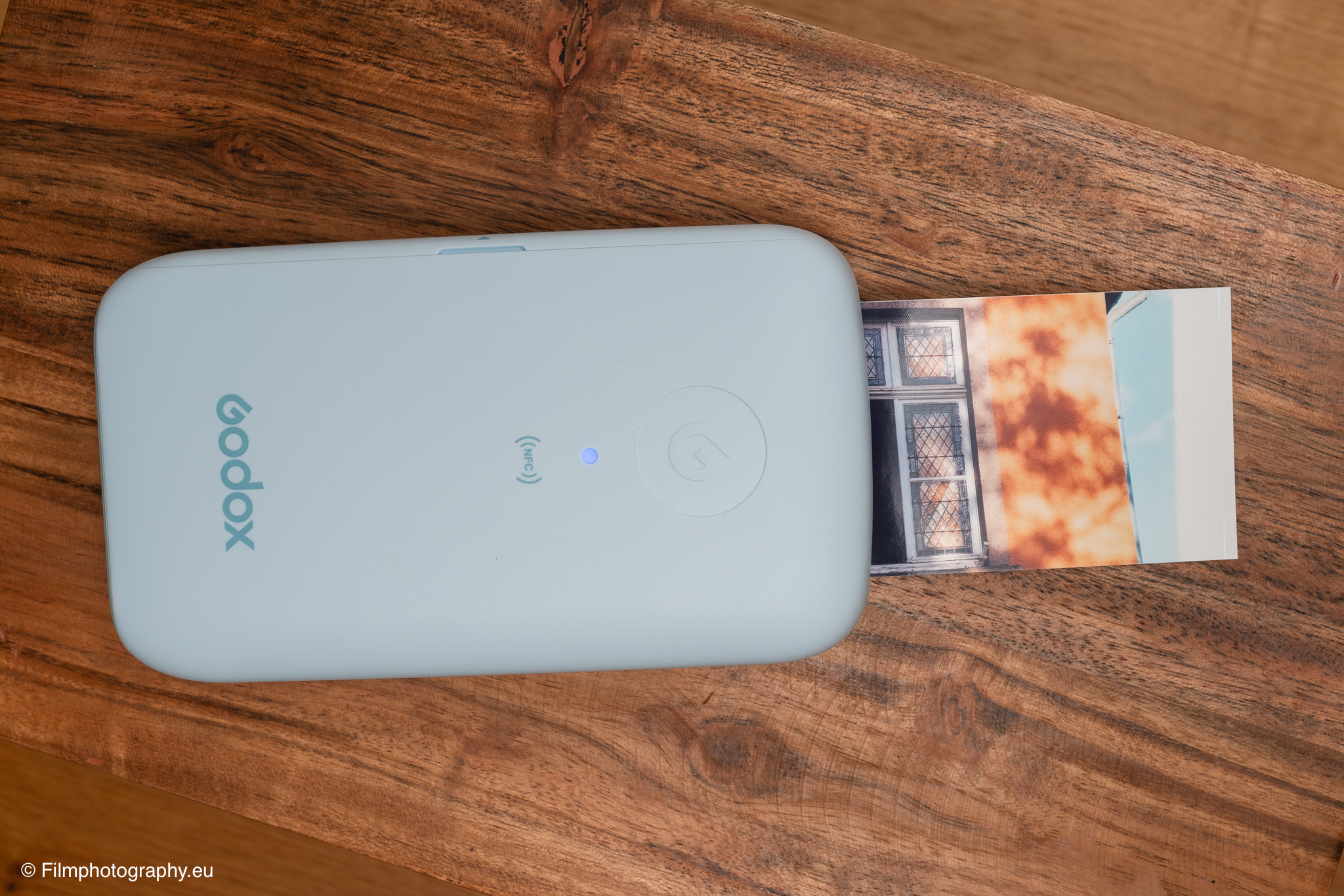 Godox P100 mobiler Drucker in Hellblau gibt einen warm getönten Ausdruck eines Fensters auf einem Holztisch aus