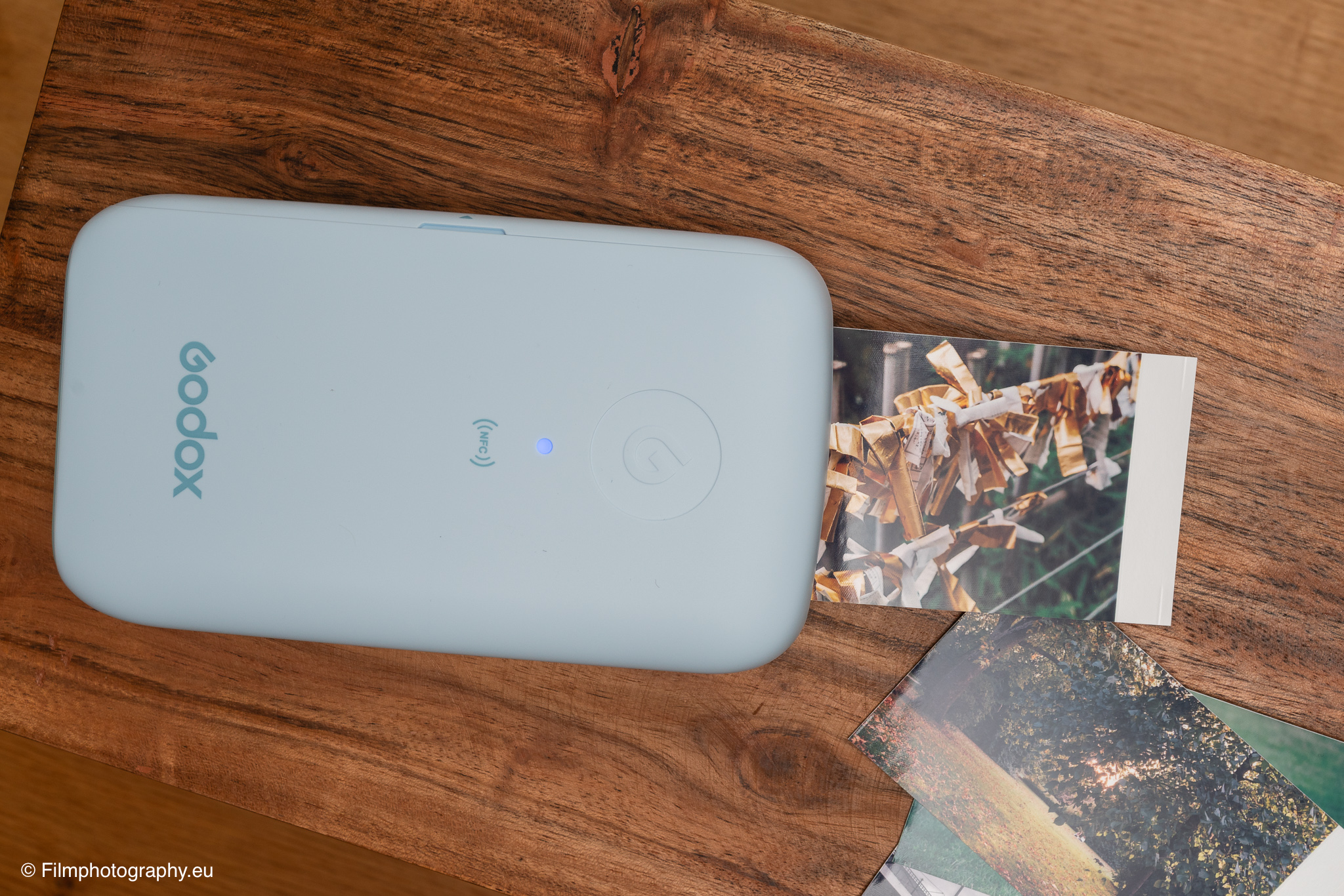 Mobiler Fotodrucker Godox P100 in Hellblau druckt während eines Tests ein Foto auf rustikalem Holztisch