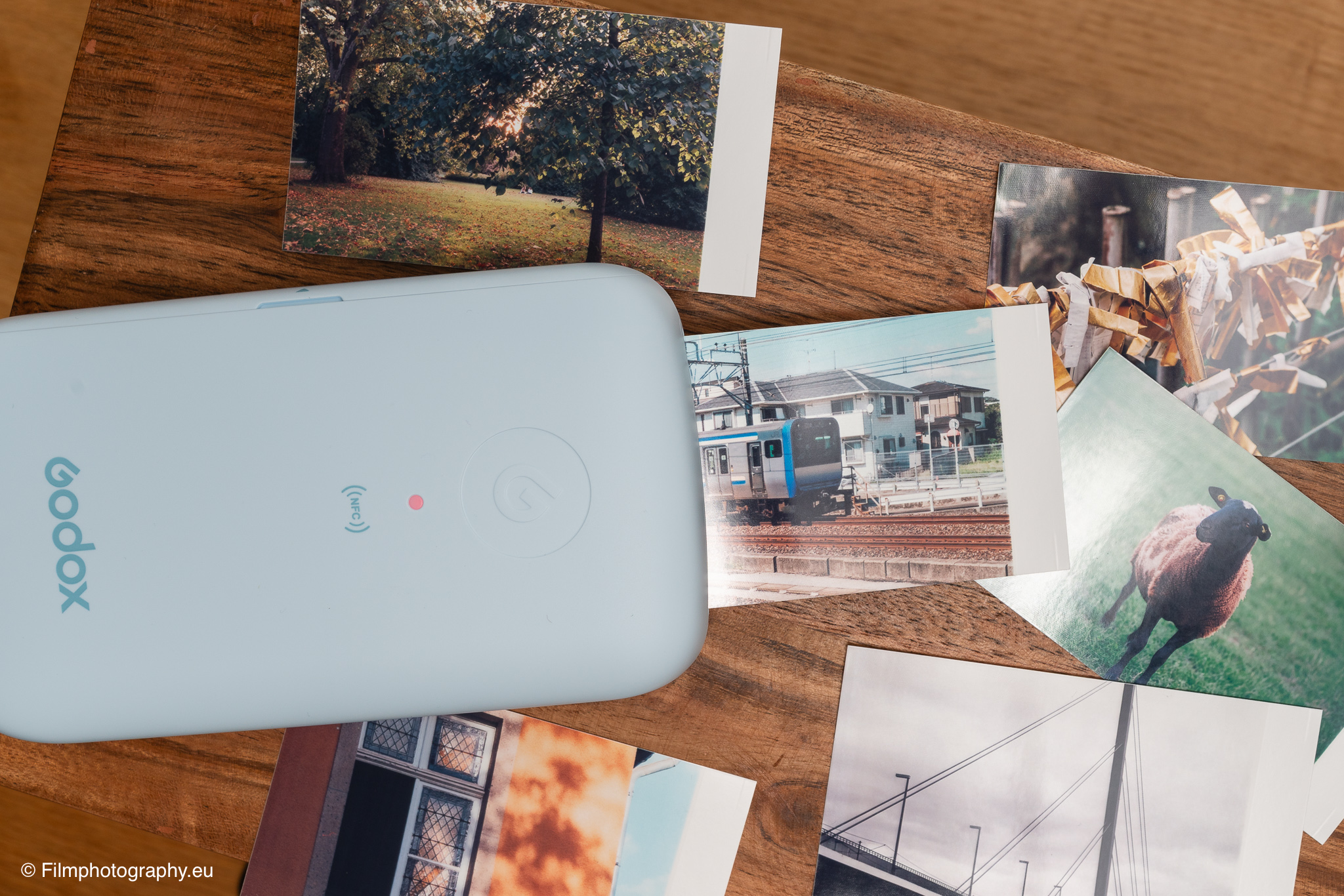 Godox P100 mobiler Fotodrucker in Hellblau druckt Sofortbilder von einem Park, Zug und Schafen auf einem Holztisch