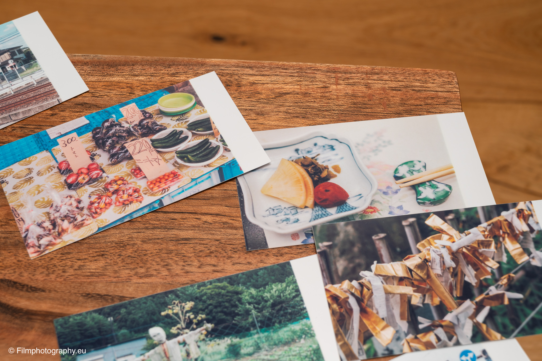 Farbige Fotoprints vom Godox P100 Mobildrucker verstreut auf einem Holztisch, zeigen japanische Marktessen und Schreinszenen.