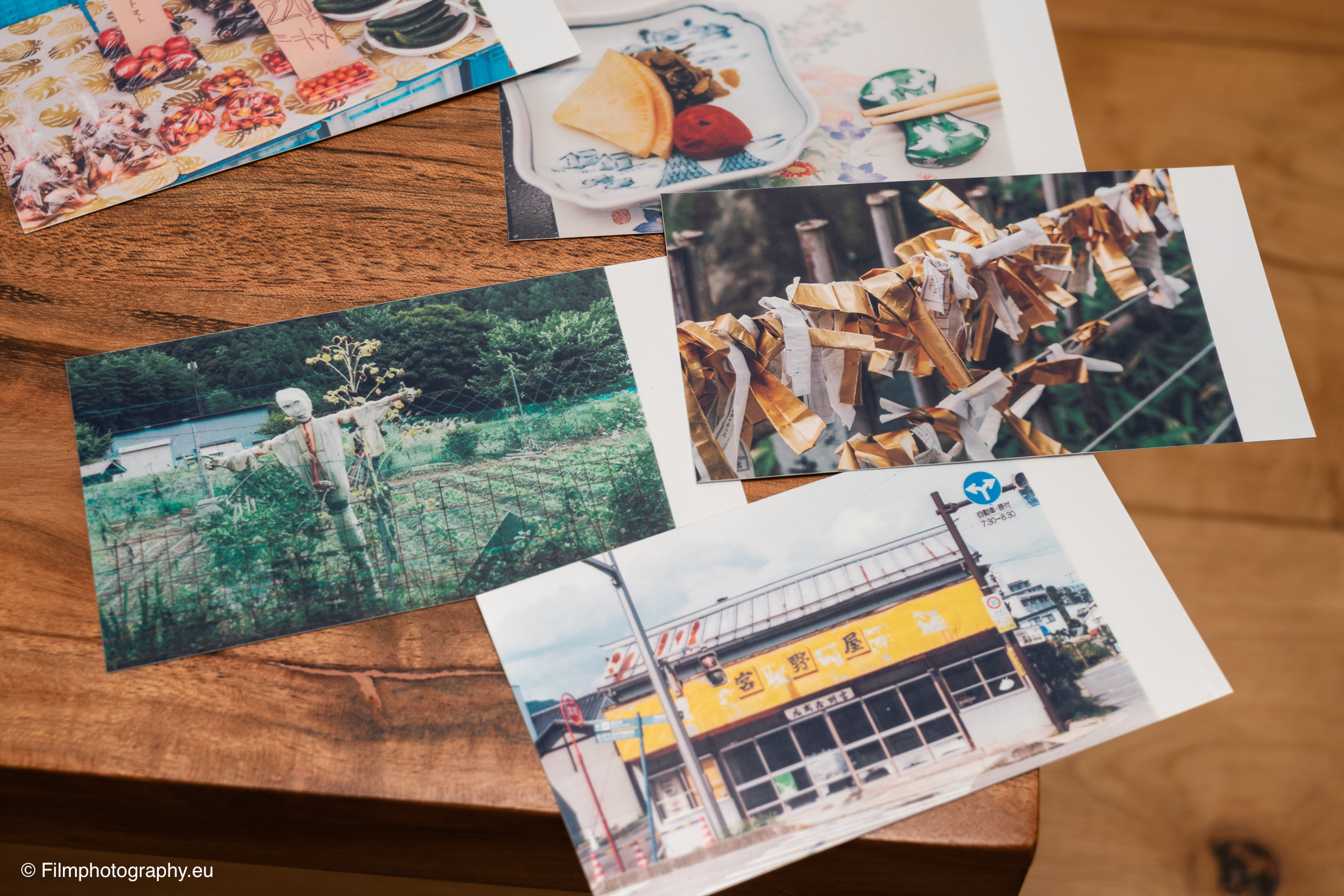 Testdrucke vom Godox P100 mobilen Drucker verstreut auf einem Holztisch, farbenfrohe japanische Szenen mit Essen, Schreinen und Straßen