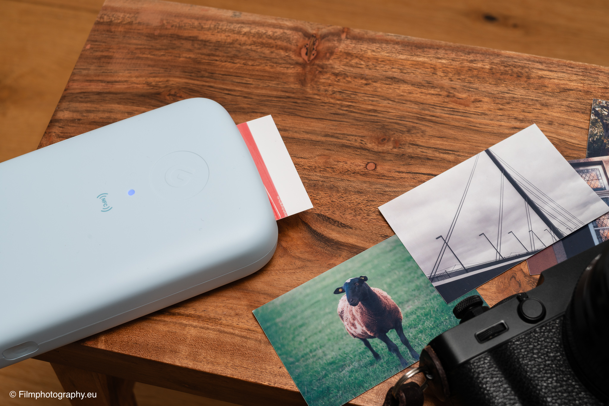 Godox P100 mobiler Fotodrucker stößt einen Ausdruck neben gedruckten Fotos eines Schafs und einer Brücke auf einem Holztisch aus