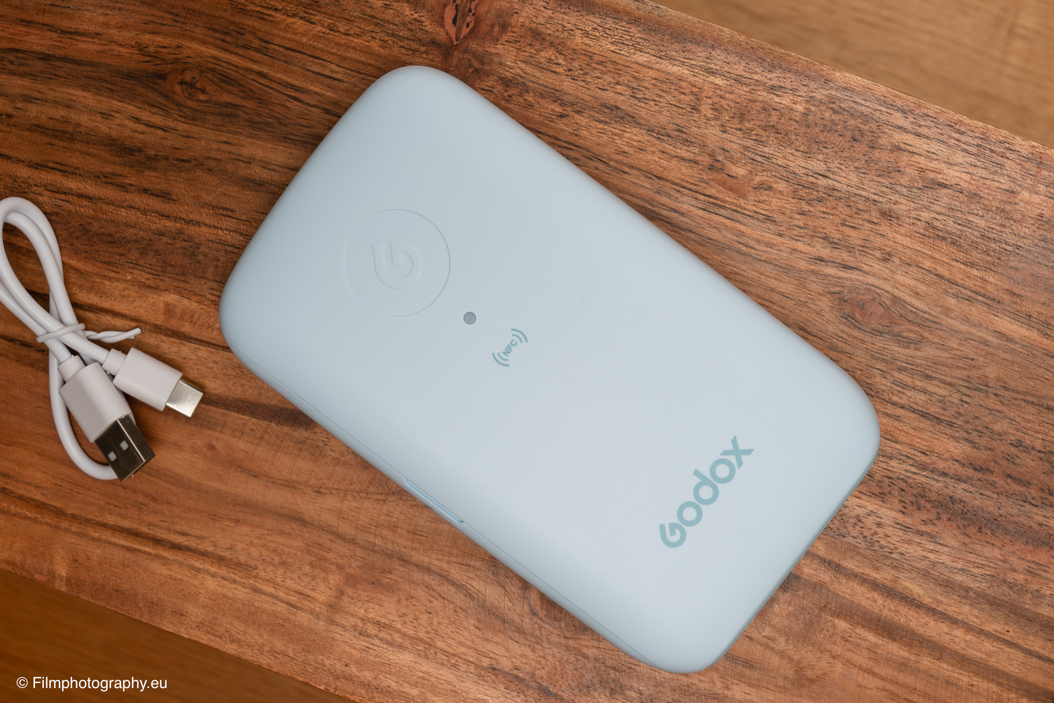 Godox P100 mobiler Fotodrucker in Hellblau mit USB-C-Kabel auf rustikalem Holztisch, Produktfoto für Testbericht.