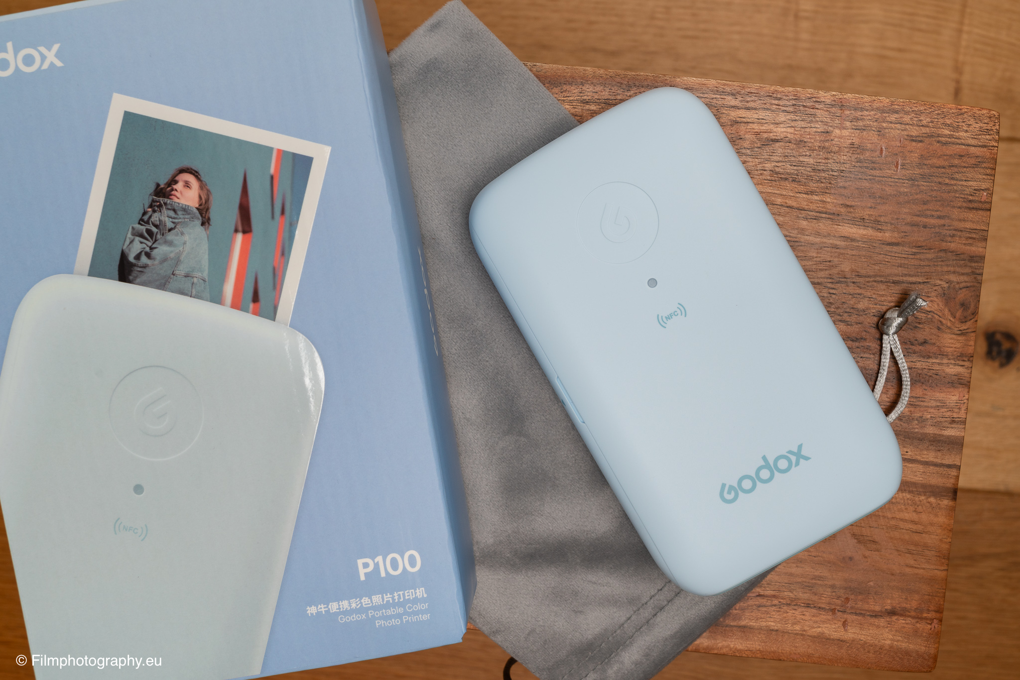 Mobiler Fotodrucker Godox P100 in Pastellblau neben der Verpackung auf Holzuntergrund, aus einem Praxistest.