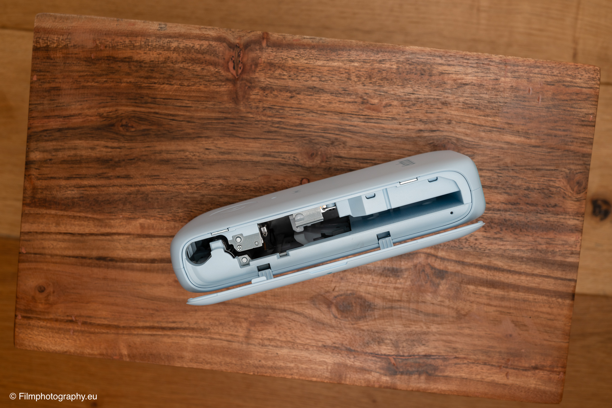 Godox P100 mobiler Fotodrucker mit geöffneter Klappe, die den internen Papiermechanismus zeigt, auf rustikalem Holztisch